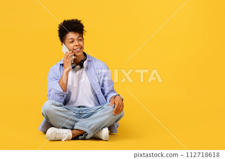 Happy black male student talking on phone with headphones on yellow background Happy black male student talking on phone with headphones on yellow background 112718618