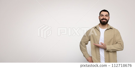 Cheerful man with a beard presenting with his hand to the side, displaying an empty space 112718676