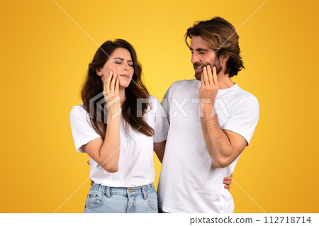 A concerned young woman and a man touch their cheeks with pained expressions 112718714