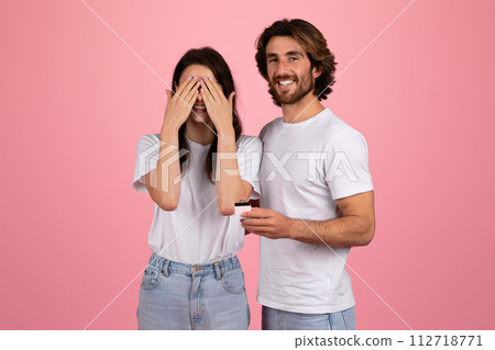 Surprised woman covering her eyes with hands and smiling man holding a small jewelry box 112718771