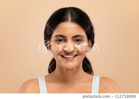 Skin Care. Young indian woman with dab of cream on her cheek Skin Care. Young indian woman with dab of cream on her cheek 112718809