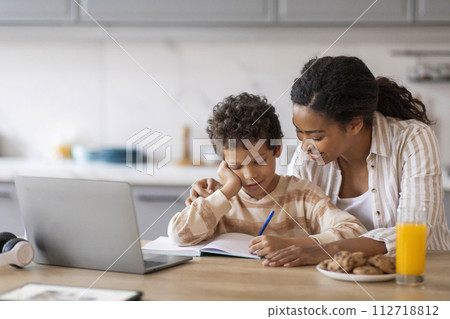 Smiling young African American mother assisting her preteen son with his schoolwork Smiling young African American mother assisting her preteen son with his schoolwork 112718812