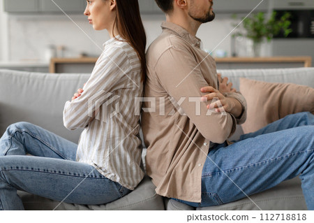 Spouses sitting on couch back to back, sulking after quarrel at home, cropped Spouses sitting on couch back to back, sulking after quarrel at home, cropped 112718818