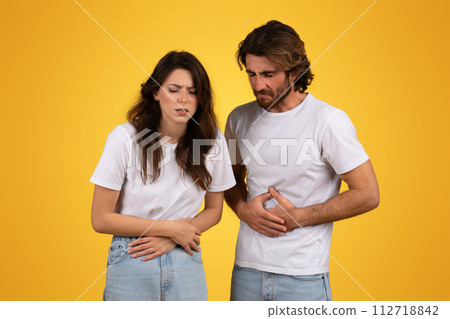 Concerned man and woman with pained expressions holding their stomachs 112718842