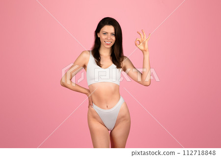 Cheerful young woman in white underwear making a perfect gesture with her hand Cheerful young woman in white underwear making a perfect gesture with her hand 112718848