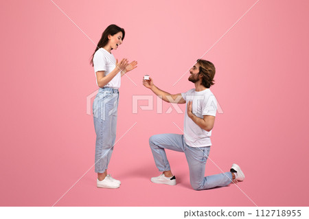 Overjoyed young woman reacts with surprise as man kneels with an engagement ring Overjoyed young woman reacts with surprise as man kneels with an engagement ring 112718955