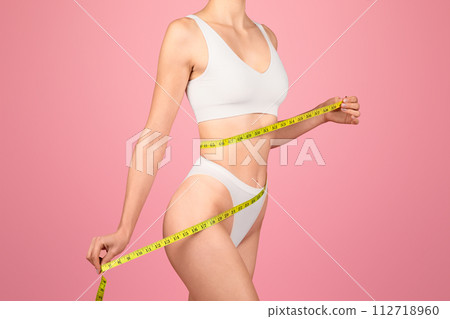 Side view of a determined woman in white lingerie measuring her perfect waist 112718960