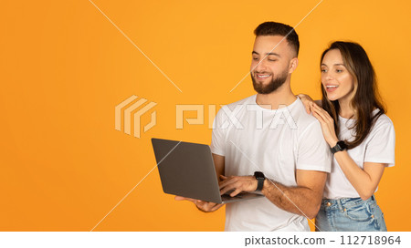 Smiling young man holding a laptop with attentive woman by his side, both wearing white t-shirts Smiling young man holding a laptop with attentive woman by his side, both wearing white t-shirts 112718964
