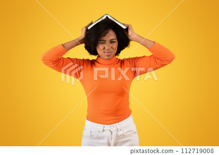 Frustrated young woman with a grimace, balancing a book on her head 112719008