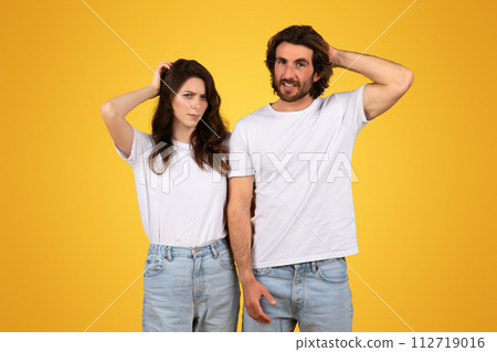 Perplexed young couple in white t-shirts and jeans, scratching their heads with puzzled expressions Perplexed young couple in white t-shirts and jeans, scratching their heads with puzzled expressions 112719016