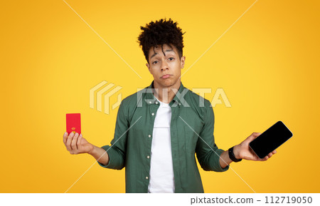 Unhappy young black guy holding phone and credit card Unhappy young black guy holding phone and credit card 112719050