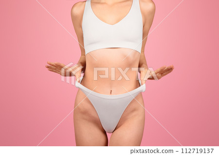 A midsection view of a woman in white sportswear, hands gesturing towards her fit abdomen A midsection view of a woman in white sportswear, hands gesturing towards her fit abdomen 112719137