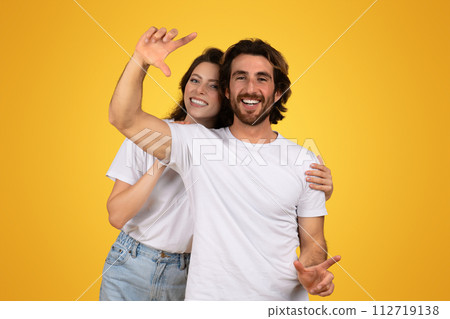 Cheerful young couple playfully gesturing towards the camera, with the woman raising her hand as if capturing a moment 112719138