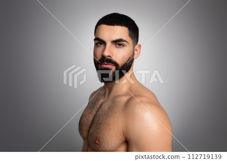 Young Middle Eastern guy with beard, shirtless, posing on grey 112719139