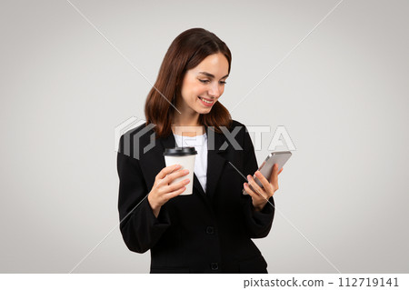 Multitasking businesswoman in a smart black suit happily checks her smartphone 112719141