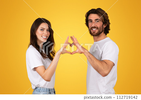 Radiant young couple creating a heart shape with their hands, smiling broadly in white t-shirts Radiant young couple creating a heart shape with their hands, smiling broadly in white t-shirts 112719142