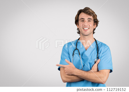 Confident male nurse in blue scrubs pointing sideways at free space with smile Confident male nurse in blue scrubs pointing sideways at free space with smile 112719152
