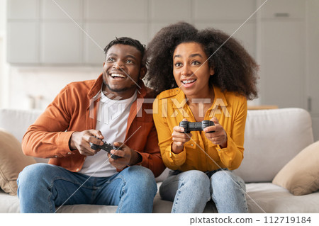 Cheerful black millennial couple playing video games at home 112719184