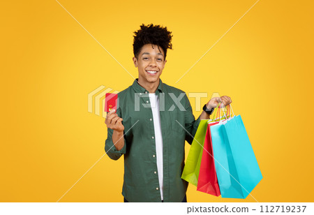 Positive african american guy showing credit card and purchases 112719237