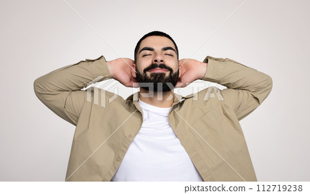 A relaxed man with a beard and a content smile leans back with his hands behind his head A relaxed man with a beard and a content smile leans back with his hands behind his head 112719238