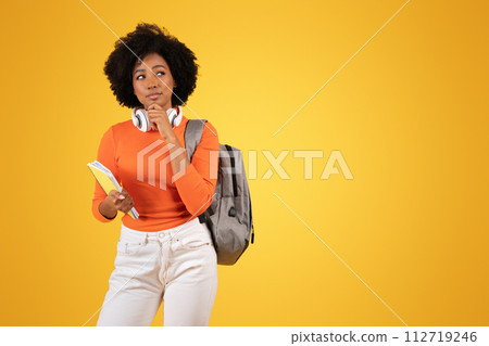 Pensive African American lady student with headphones and a gray backpack looks away 112719246