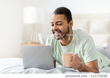 Happy african american man using laptop in bed, copy space 112719290