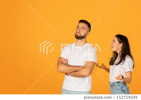 Skeptical man with crossed arms looking unconvinced beside a talking woman Skeptical man with crossed arms looking unconvinced beside a talking woman 112719295