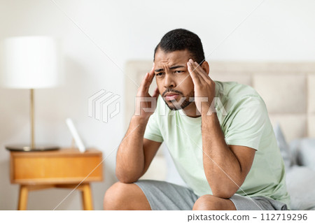 Closeup african american guy sitting on bed, touching his head 112719296