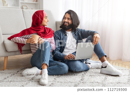 Cheerful Muslim Couple Relaxing Together With Laptop And Coffee In Living Room 112719300