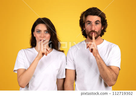 A young woman and a man with dark hair and white t-shirts gesture for silence 112719302
