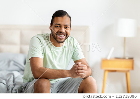 Positive african american guy sitting on bed after waking up Positive african american guy sitting on bed after waking up 112719390