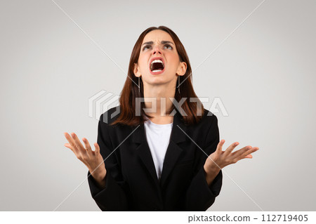 Desperate businesswoman in a black suit looking upwards with hands raised in exasperation 112719405