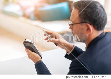 A mature businessman in a smart suit uses contactless payment with his smartphone A mature businessman in a smart suit uses contactless payment with his smartphone 112719459