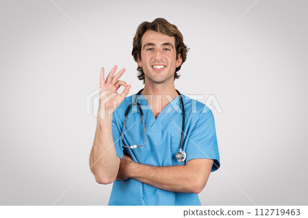 Confident man nurse in blue scrubs giving positive ok gesture Confident man nurse in blue scrubs giving positive ok gesture 112719463