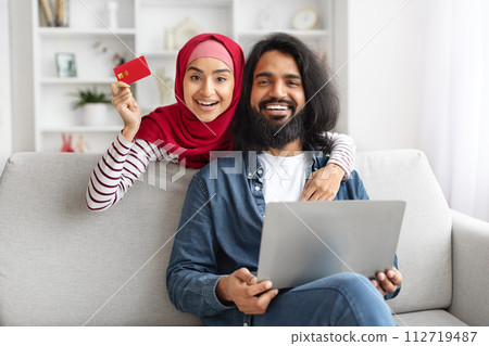Online Shopping. Happy Muslim Couple Using Laptop And Credit Card At Home, Online Shopping. Happy Muslim Couple Using Laptop And Credit Card At Home, 112719487