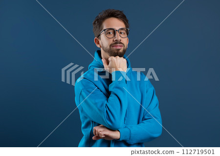 Pensive man wearing eyeglasses resting chin on hand and looking at camera 112719501