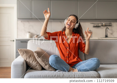 Happy woman with headphones enjoying music on her couch 112719509