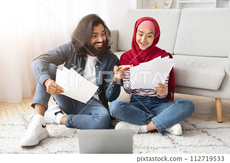 Happy young muslim couple checking documents while sitting on floor at home 112719533