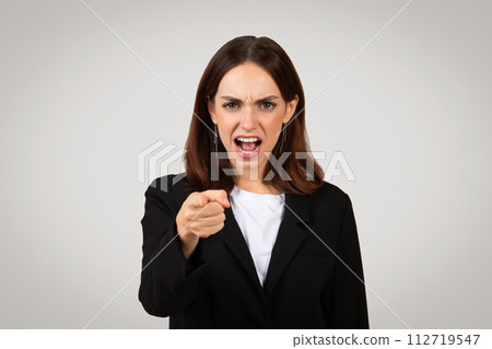 Frustrated businesswoman in black attire angrily pointing forward, displaying a strong expression of blame Frustrated businesswoman in black attire angrily pointing forward, displaying a strong expression of blame 112719547