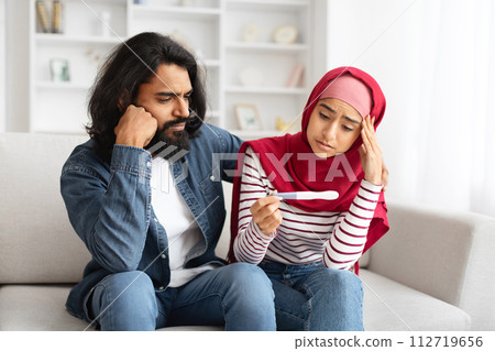 Upset muslim couple with negative pregnancy test sitting on couch at home 112719656