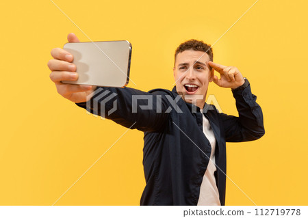 Charismatic young guy taking selfie on smartphone, yellow background 112719778