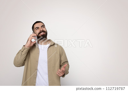 Confident young man with a full beard engaging in a pleasant conversation on a mobile phone Confident young man with a full beard engaging in a pleasant conversation on a mobile phone 112719787