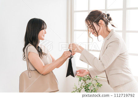 一名店員/銷售人員和一名女性購物者在奢侈品店(百貨公司、百貨公司、品牌商品)遞紙袋和產品 一名店員/銷售人員和一名女性購物者在奢侈品店(百貨公司、百貨公司、品牌商品)遞紙袋和產品 112719792