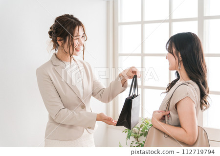一名店員/銷售人員和一名女性購物者在奢侈品店（百貨公司、百貨公司、品牌商品）遞紙袋和產品 112719794