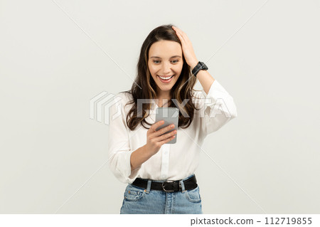 Surprised and delighted woman looking at her smartphone with one hand on her head 112719855