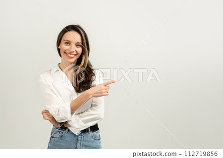 Confident and smiling young brunette woman in a white blouse pointing to the side Confident and smiling young brunette woman in a white blouse pointing to the side 112719856