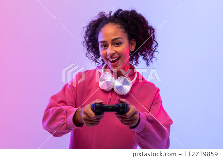 Excited young female gamer with headphones playing with controller Excited young female gamer with headphones playing with controller 112719859