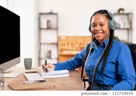 Confident black student lady with headphones studying at her desk 112719954