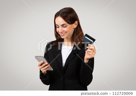 Content businesswoman holding a credit card and smartphone, possibly making an online purchase 112720009