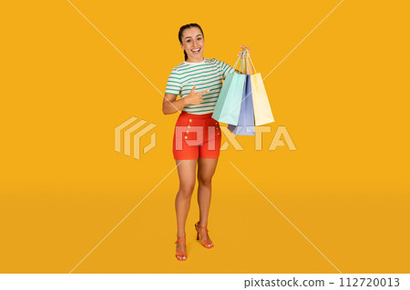 Pretty young woman pointing at shopping bags in her hand 112720013